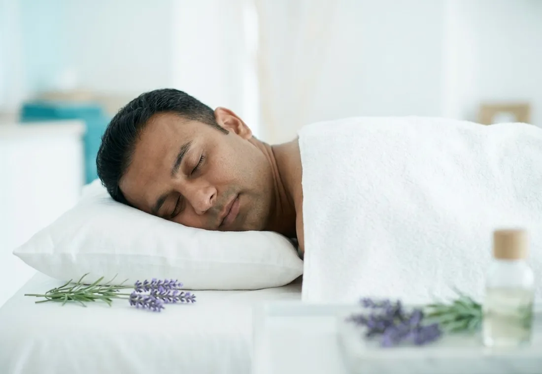 Client asleep on a white pillow with lavender sprigs and an aroma oil bottle beside him